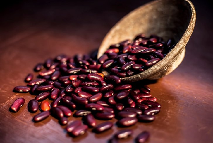 Close up of raw kidney beans on brown colored surface in a clay bowl with a spotlight on it. Horizontal shot.