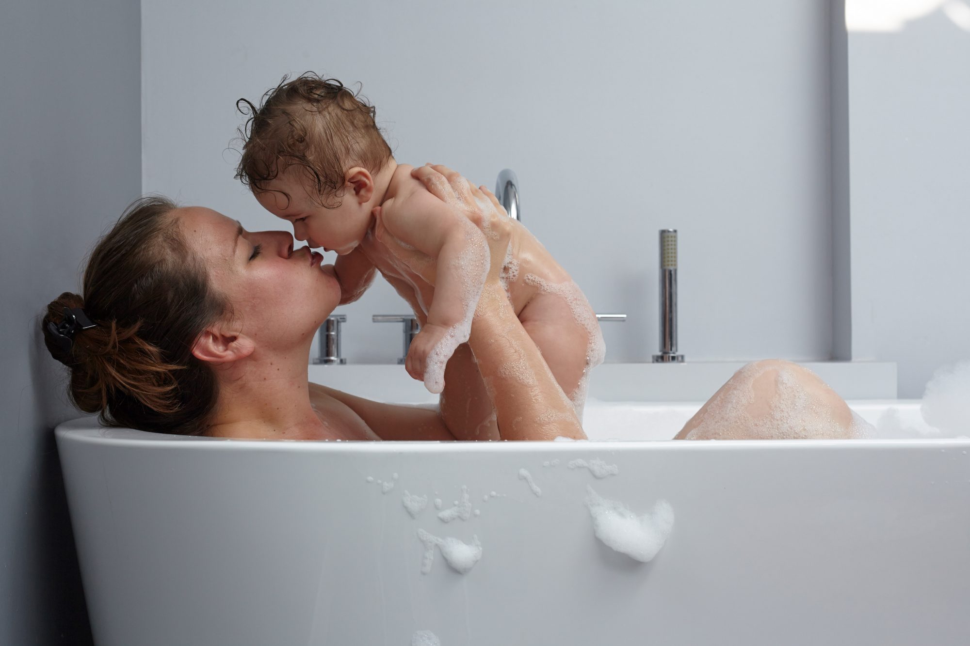 An image of mom holding her baby in a bathtub.