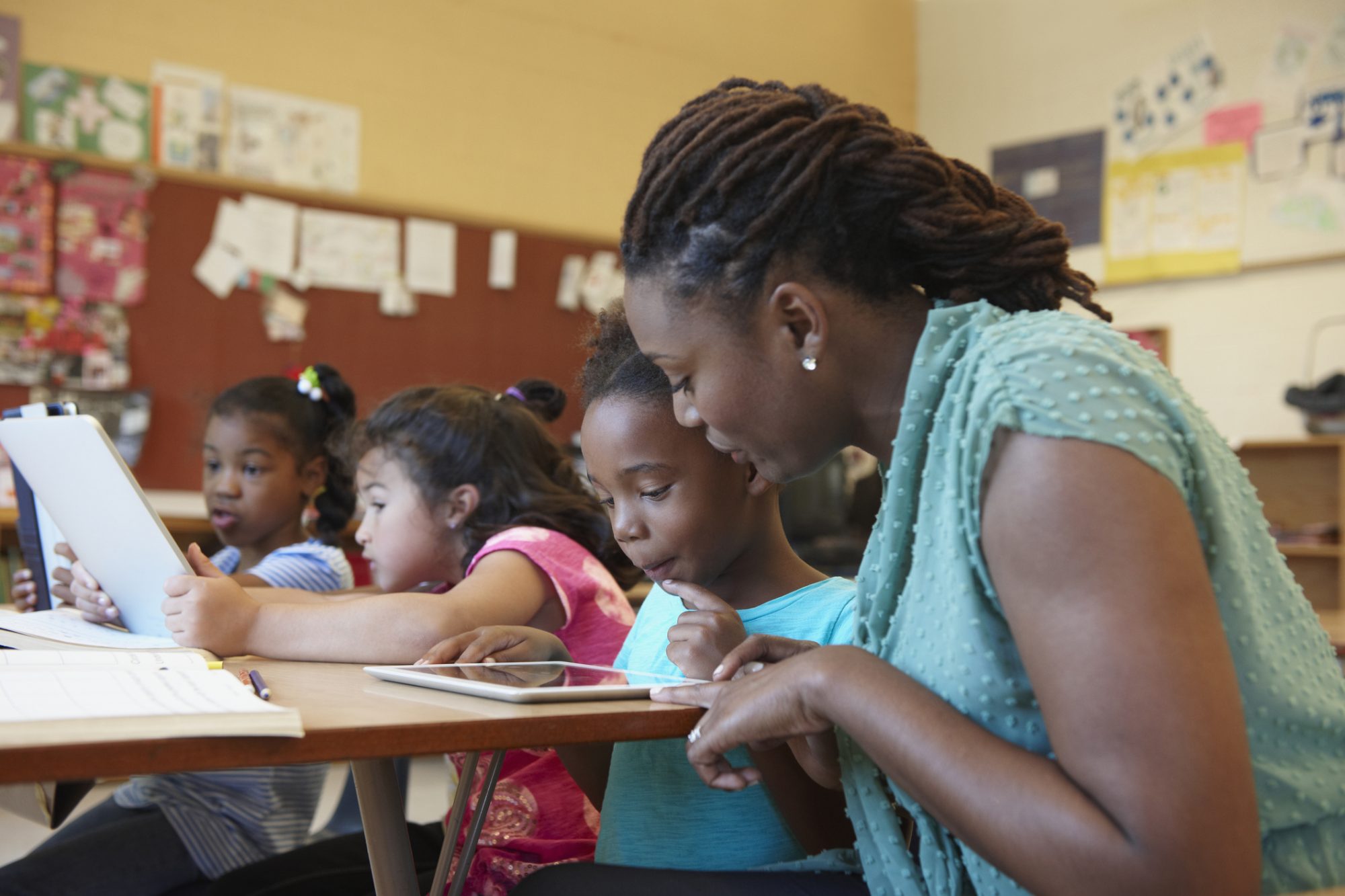 An image of a teacher helping a student with a tablet.