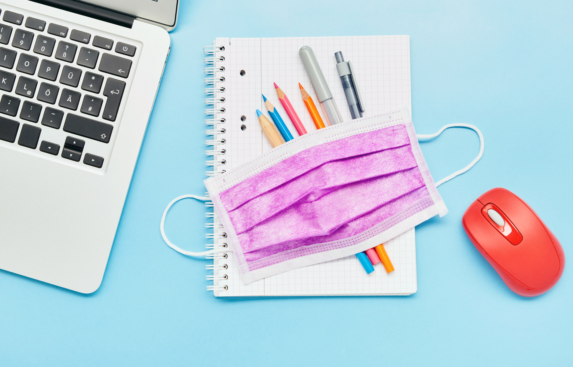 An image of school supplies and a laptop with a mask.