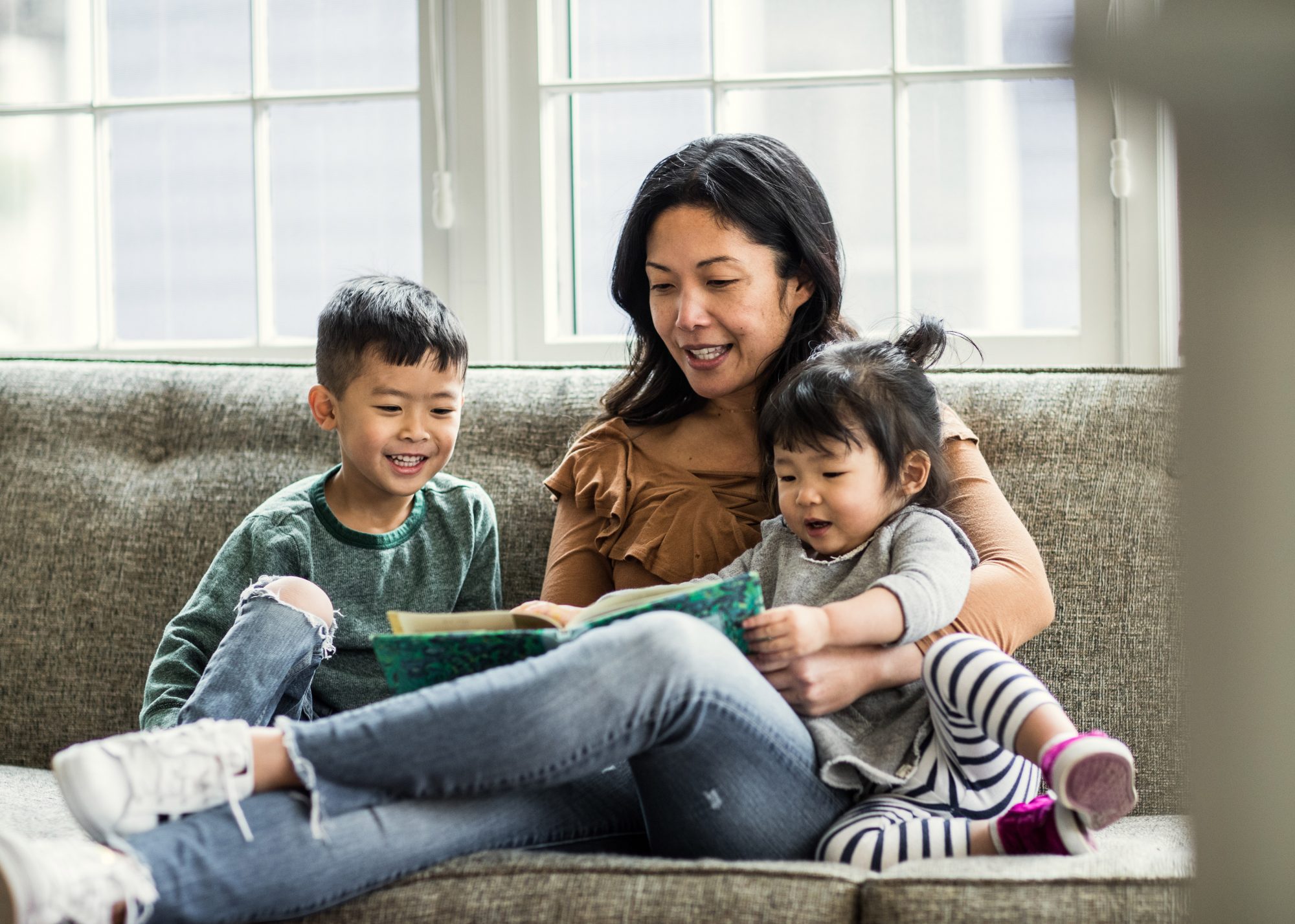 An image of a mom reading to her kids on a couch.